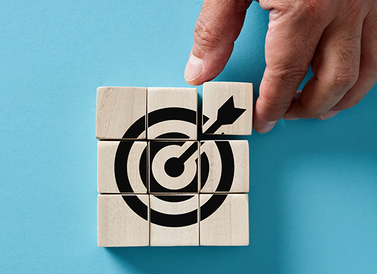 A hand completes a wooden puzzle forming a target, symbolizing goal-setting and achieving milestones in retirement planning.